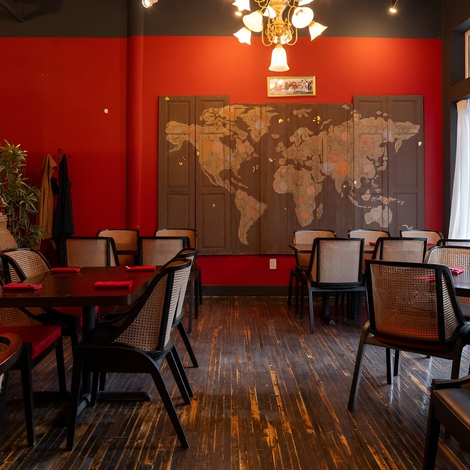 Restaurant dining room with red walls, dark wood floors, cane-back chairs, and a world map mural.