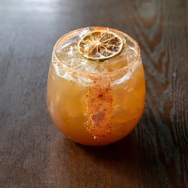 A spiced cocktail with a dried lime slice and ice, on a dark wooden table.
