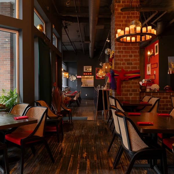 Restaurant interior with dark wood tables, wicker chairs, red walls, and a large window overlooking a street.