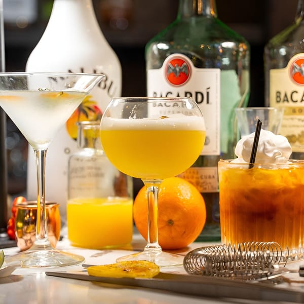 Three colorful cocktails, a martini, a yellow drink, and a brown drink with whipped cream, on a bar.
